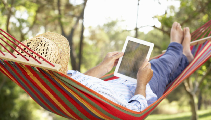 Senior Man Relaxing In Hammock With E-Book